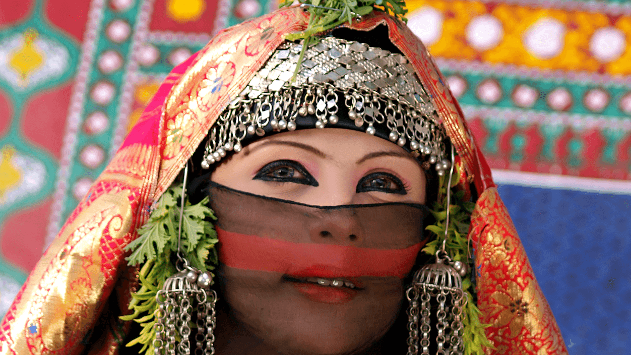 Beduinka obučena u &scaron;arenu, mahom crvenu garderobu, prekrivene glave i lica &scaron;arenom providnom tkaninom i metalnim ukrasima sa obe strane, obojenih očiju kajalom