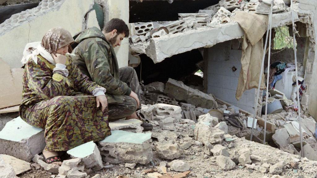 Libanski &scaron;iitski borac Hezbolaha sedi sa majkom pored njihove uni&scaron;tene kuće u Sidikinu,</figure></div>