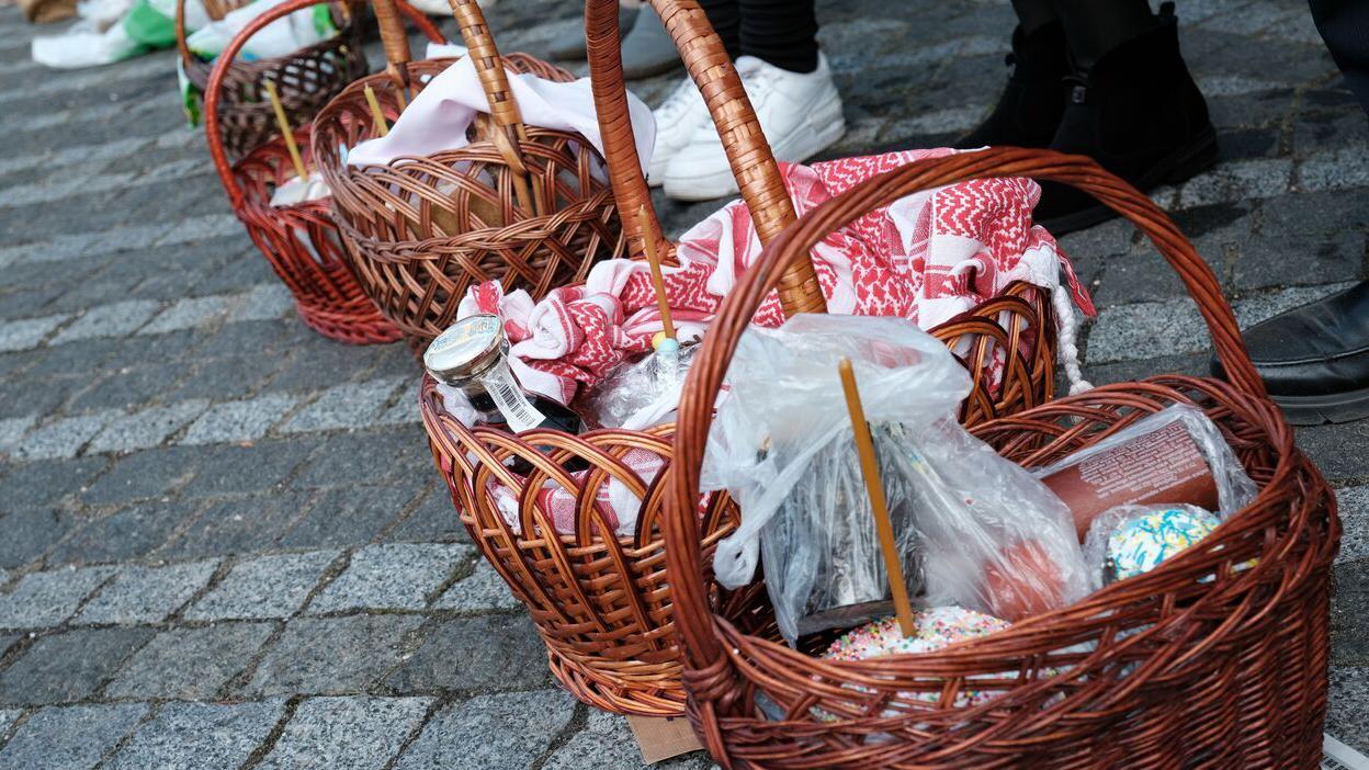 Nekoliko drvenih korpa na pločniku sa uskr&scaron;njom hranom, svećama i maramama