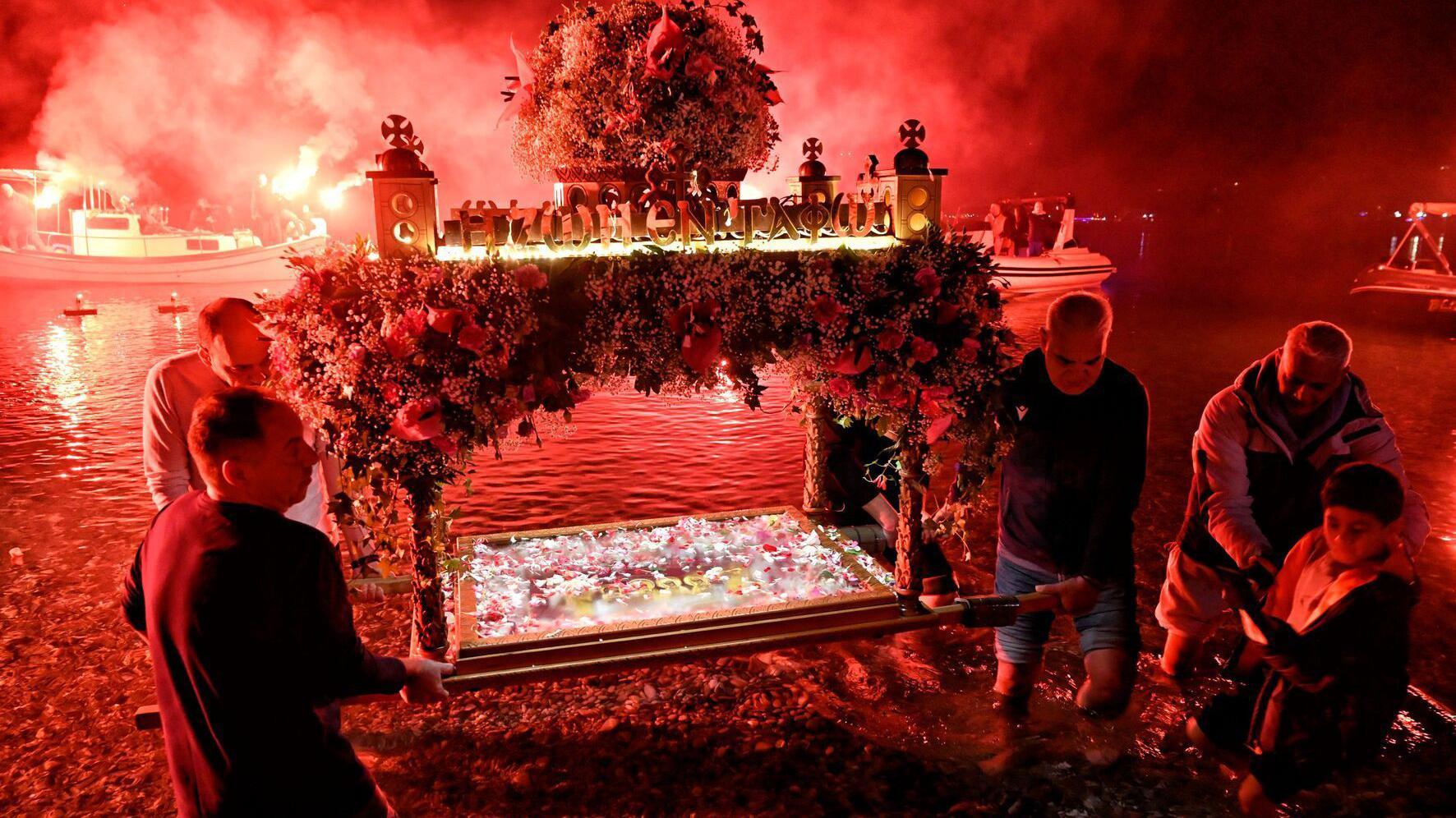 Nekoliko mu&scaron;karaca nosi ukra&scaron;eno drveno postoje kroz vodu dok je iza njih vatromet